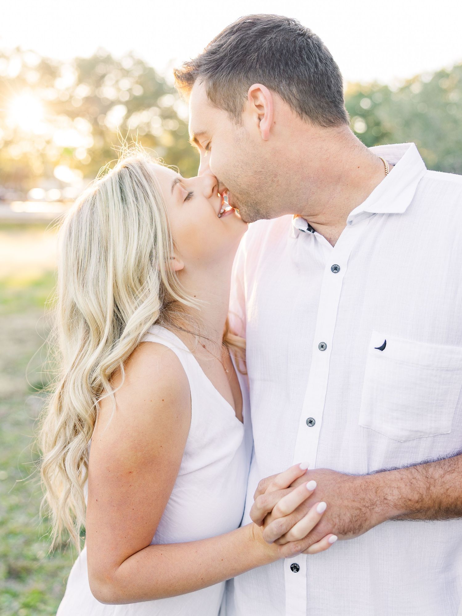 Two people in white clothing share intimate embraces during a golden hour photoshoot.