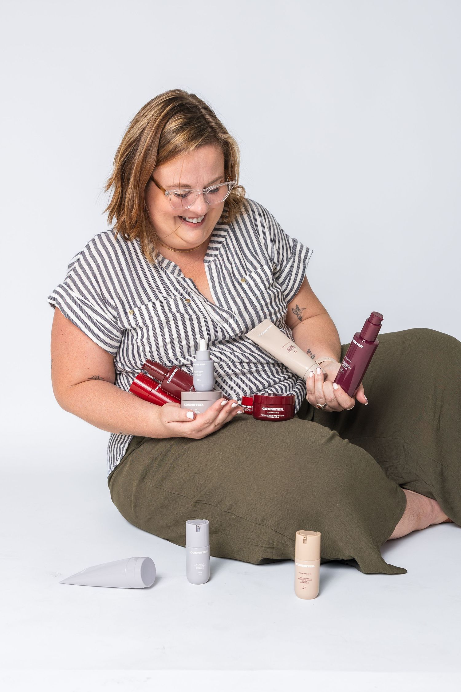 Person in striped shirt sitting with beauty products on white background.