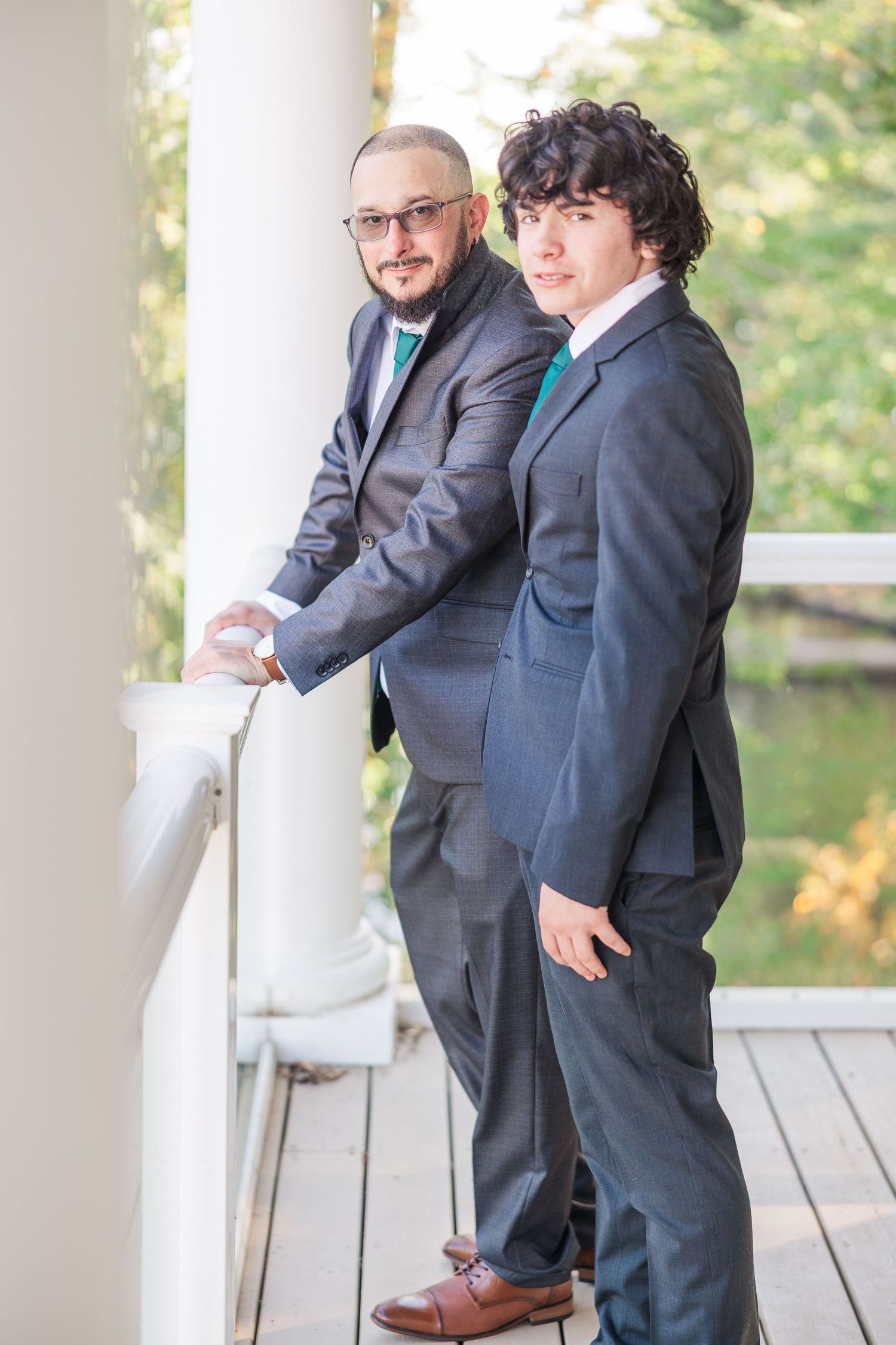 Two people in suits stand together on a white porch with natural lighting wedding groom bride lake Gaston photographer light airy