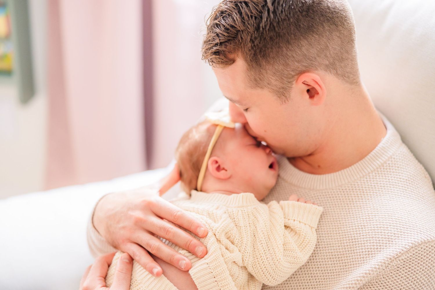 Intimate portrait of parent cradling newborn in cream sweater.