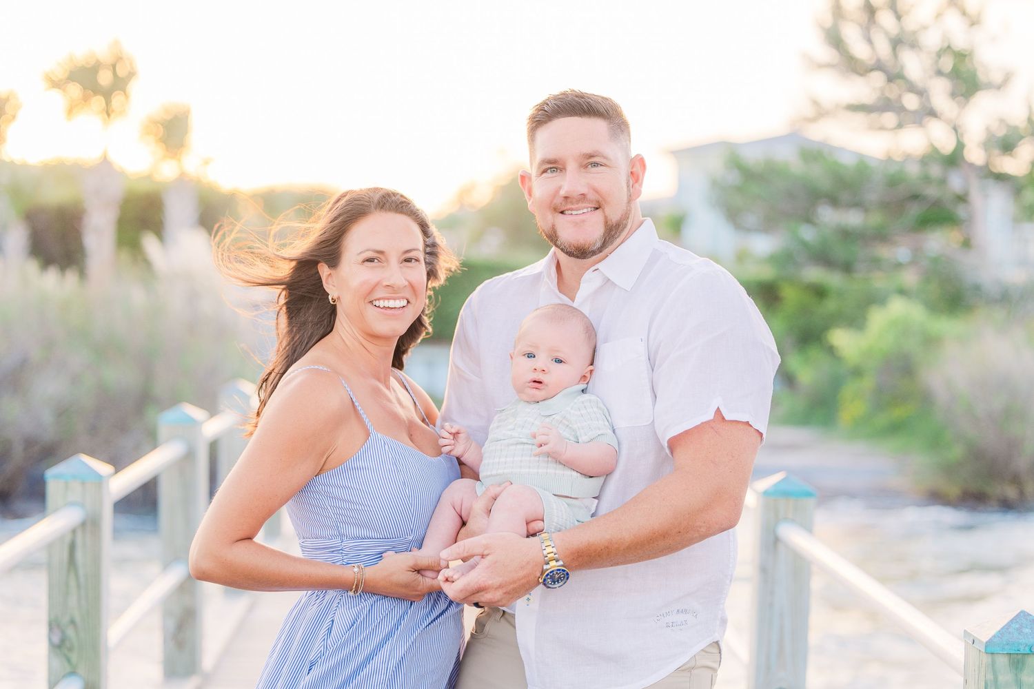 A family shares a joyful moment together with their baby on a wooden pier at sunset.