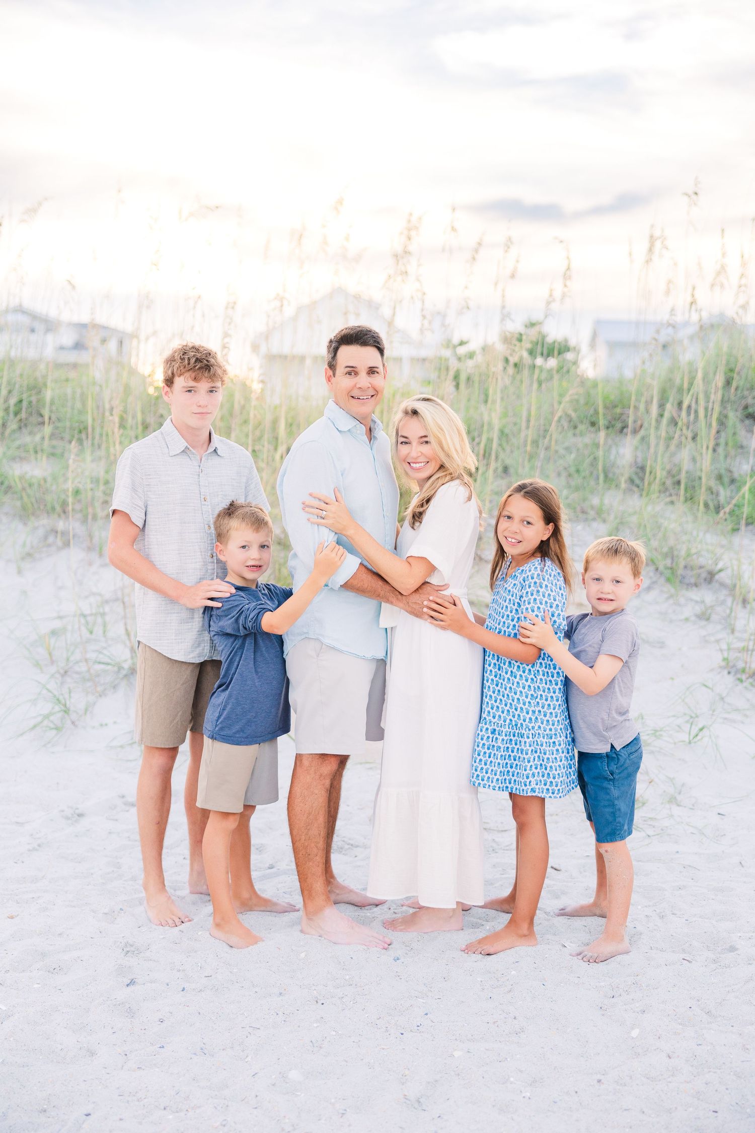 Group photo of a family wearing coordinated blue and white outfits on a sandy beach.
