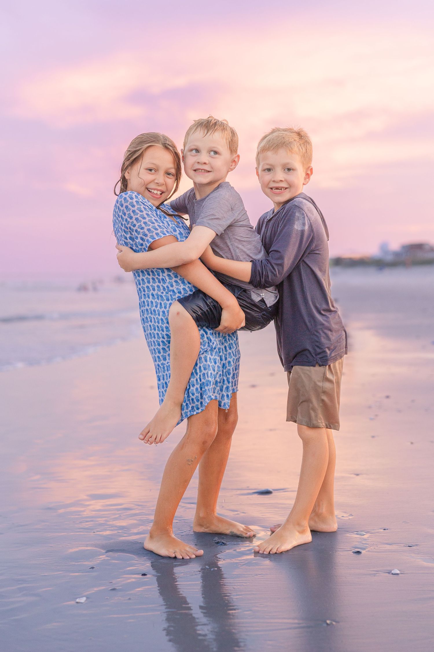 Three children playing and laughing together on the beach during sunset.