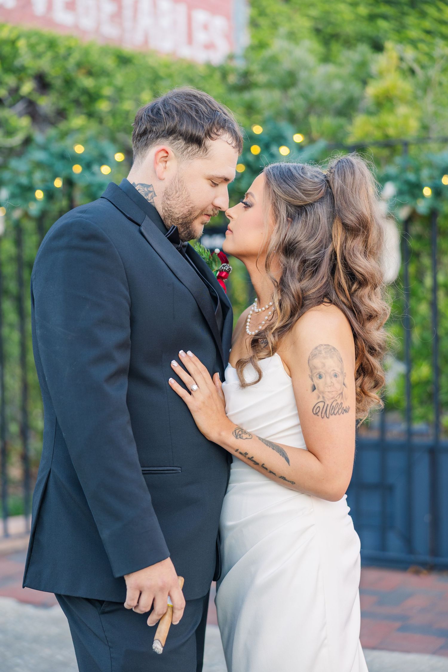 Romantic outdoor wedding couple sharing intimate moments in front of a garden setting with twinkle lights.