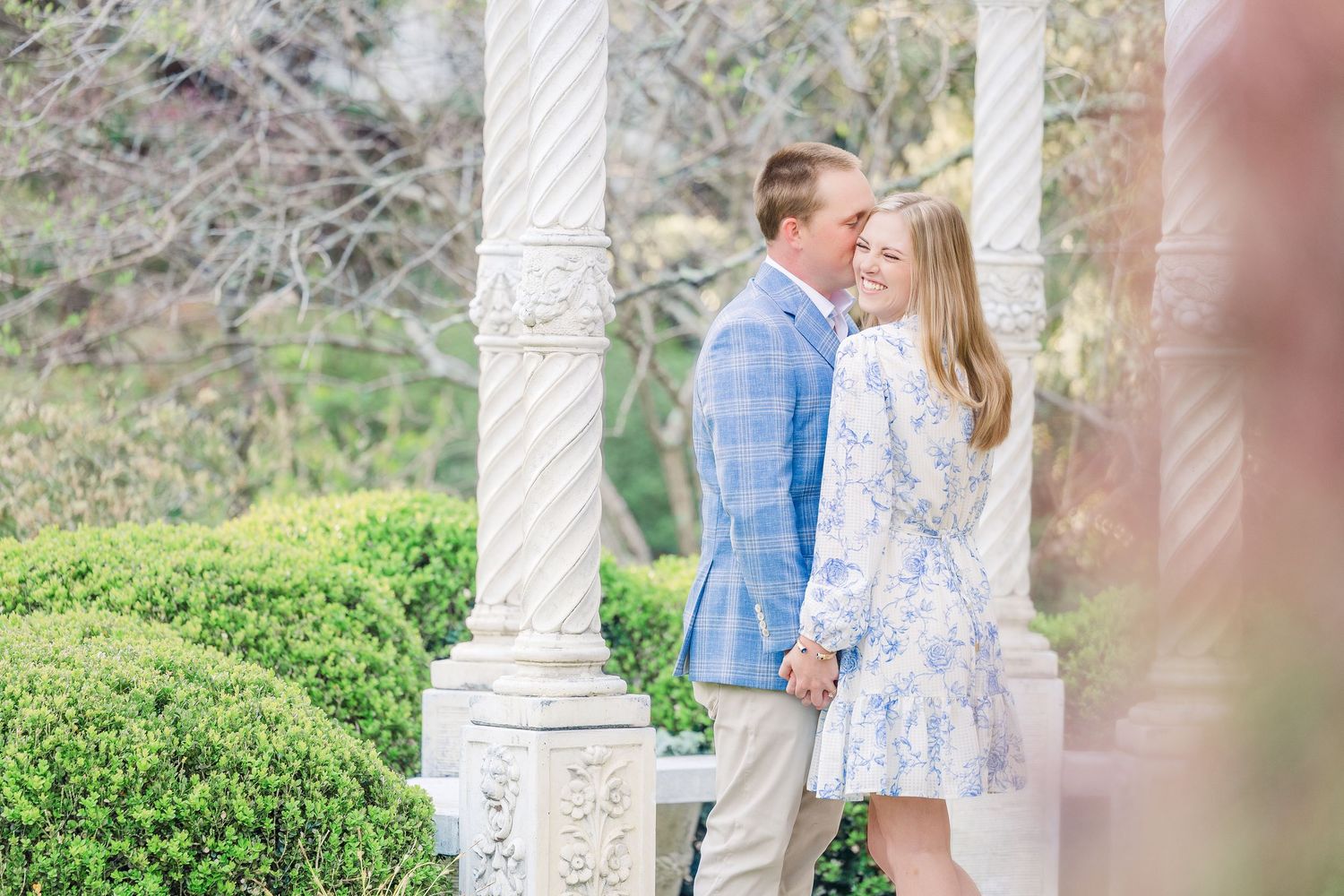 A couple shares a romantic moment in a garden gazebo surrounded by lush greenery and white columns.