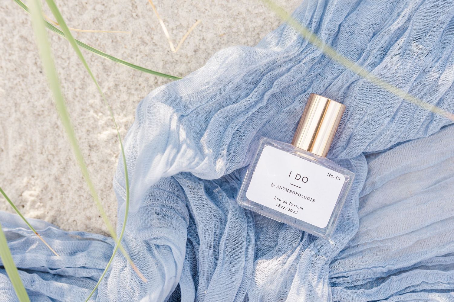A bottle of I Do perfume by Pinrose resting on a blue chiffon fabric outdoors in Carolina Beach near Wilmington, NC.
