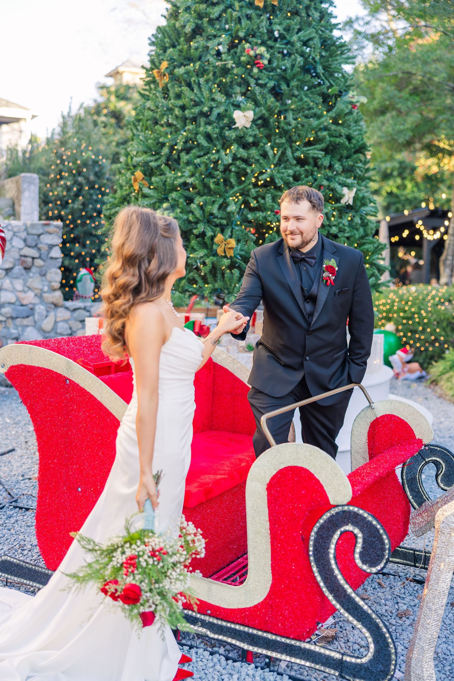 Festive holiday wedding scene with decorated Christmas trees and red sleigh prop.