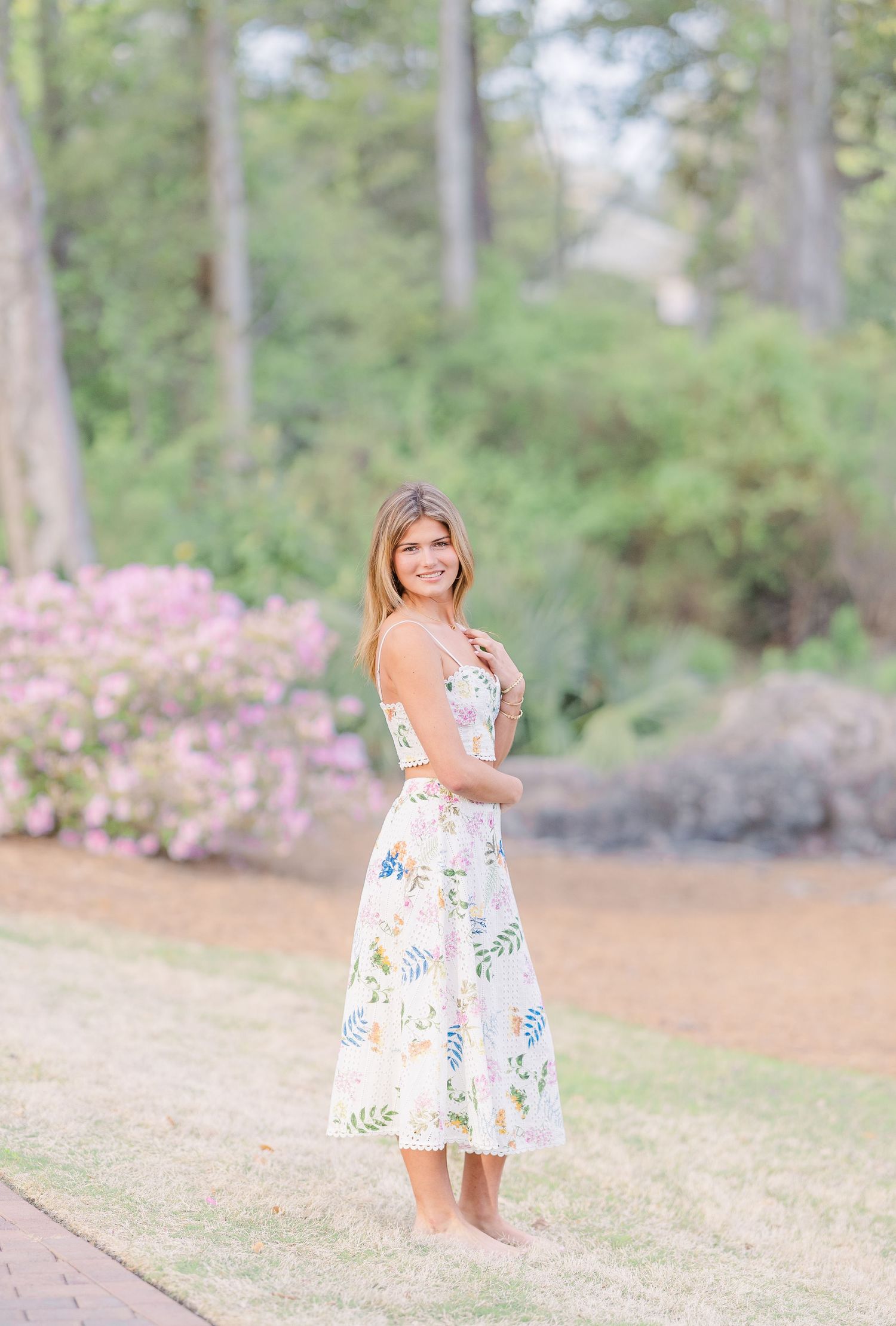 Floral dress photoshoot in a garden setting with blooming azaleas and tall pine trees.