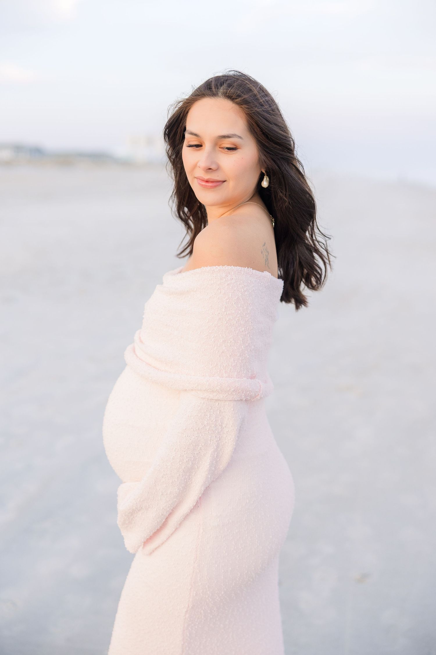 Woman in a soft pink wrap poses gracefully on a misty beach during sunset.