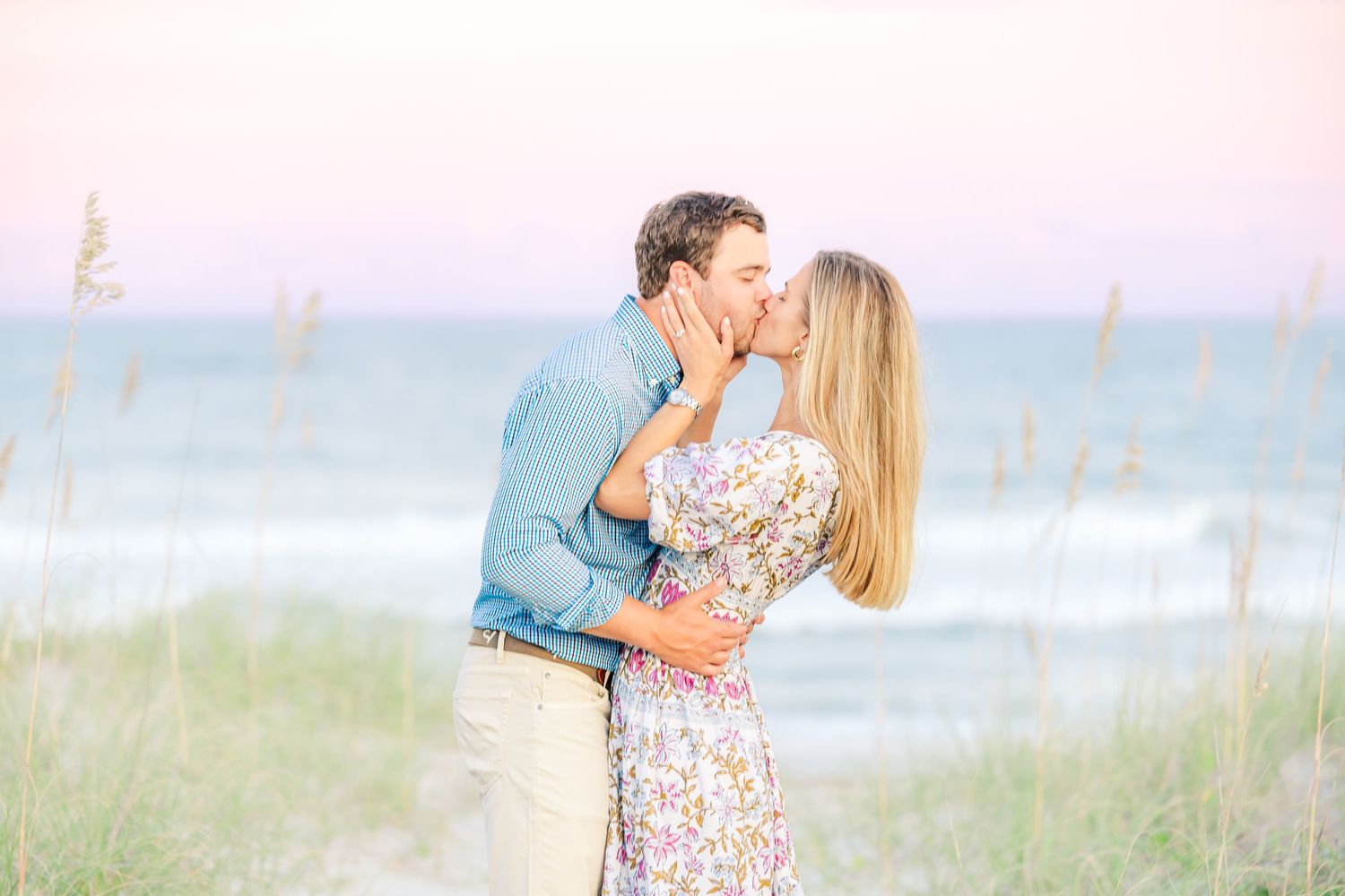 Romantic beach photoshoot with couple in coordinated outfits against pastel sky.