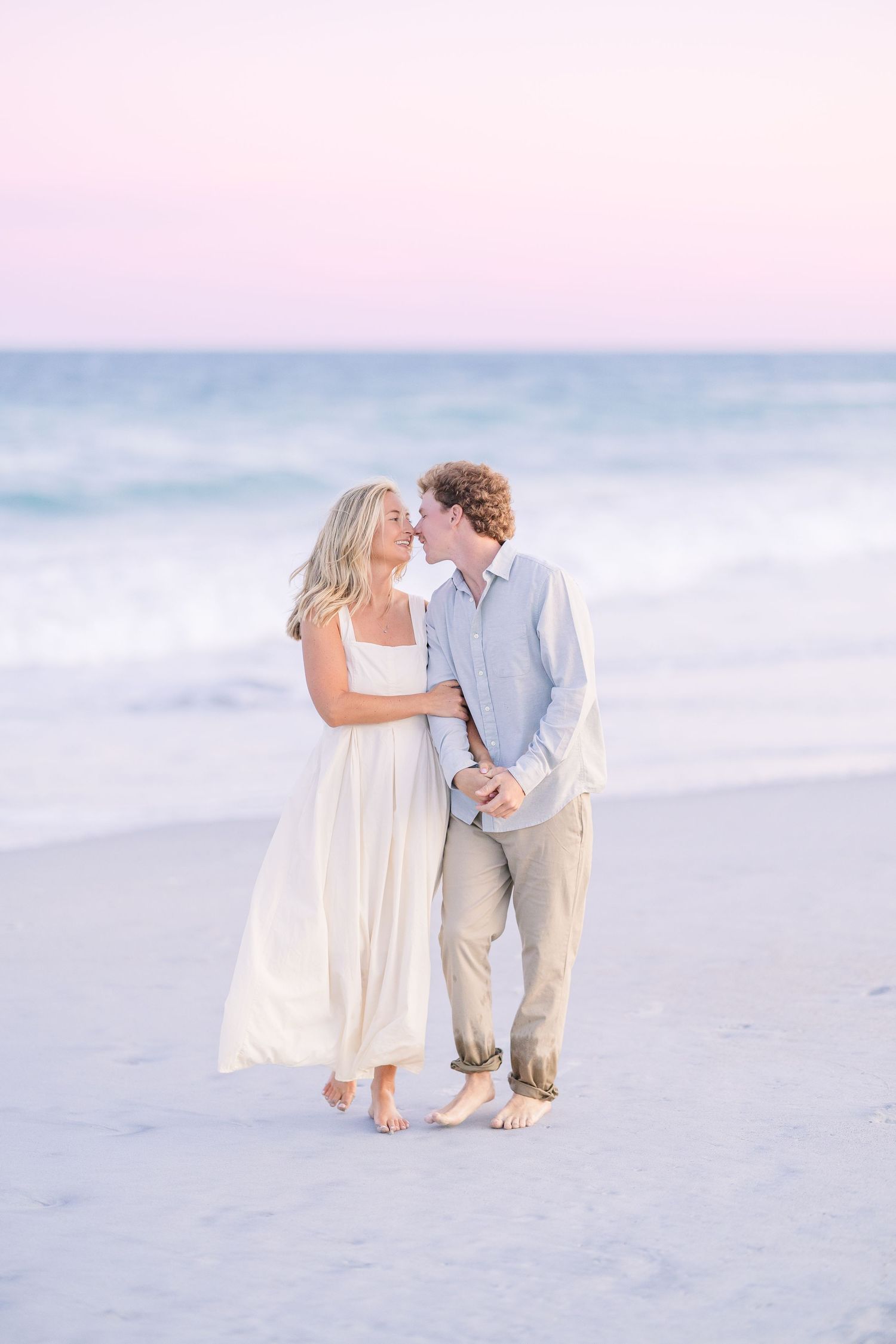 Intimate beach portraits of a couple in coordinated white and beige outfits against pastel sunset colors.