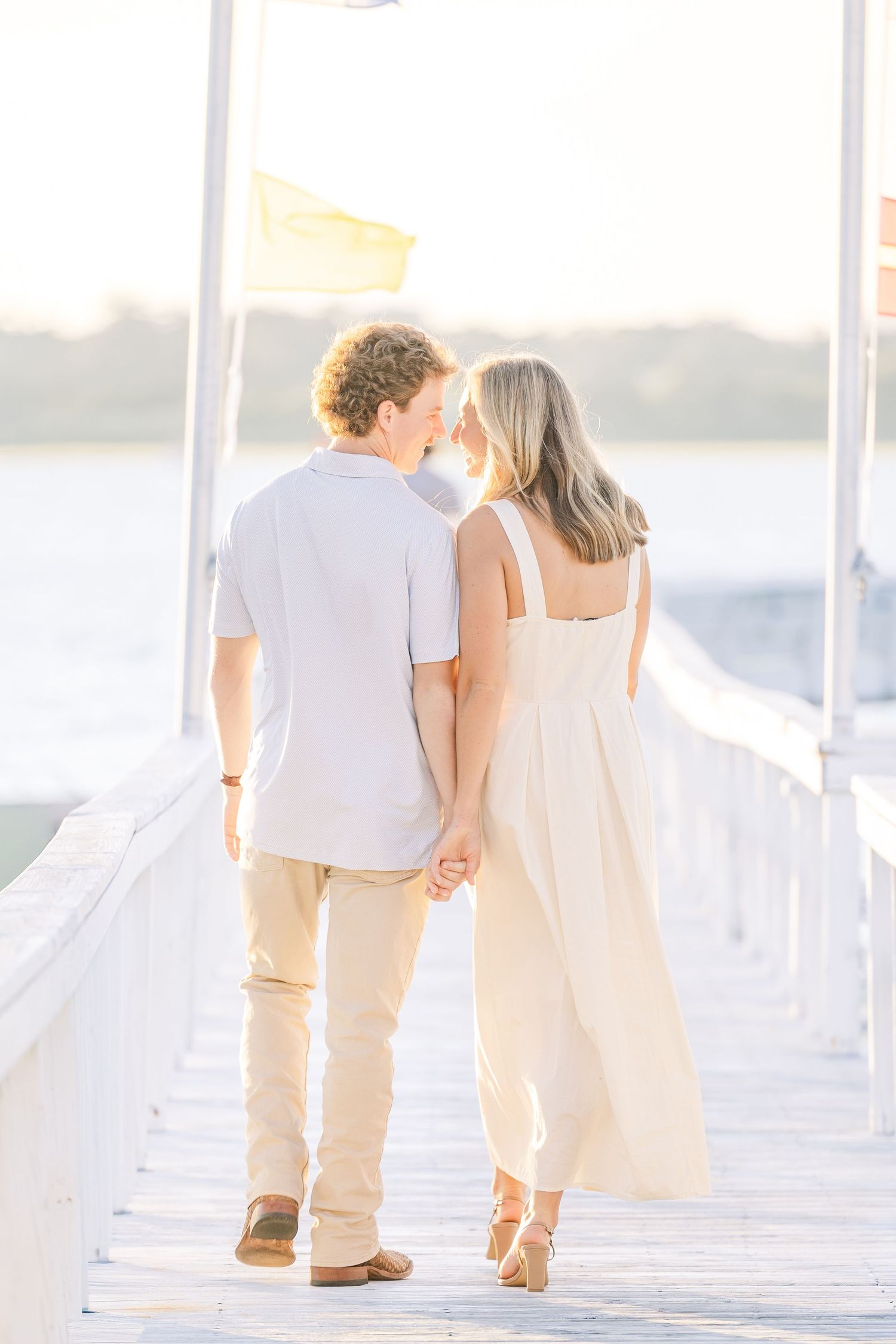 A couple walks hand in hand on a white dock during golden hour.