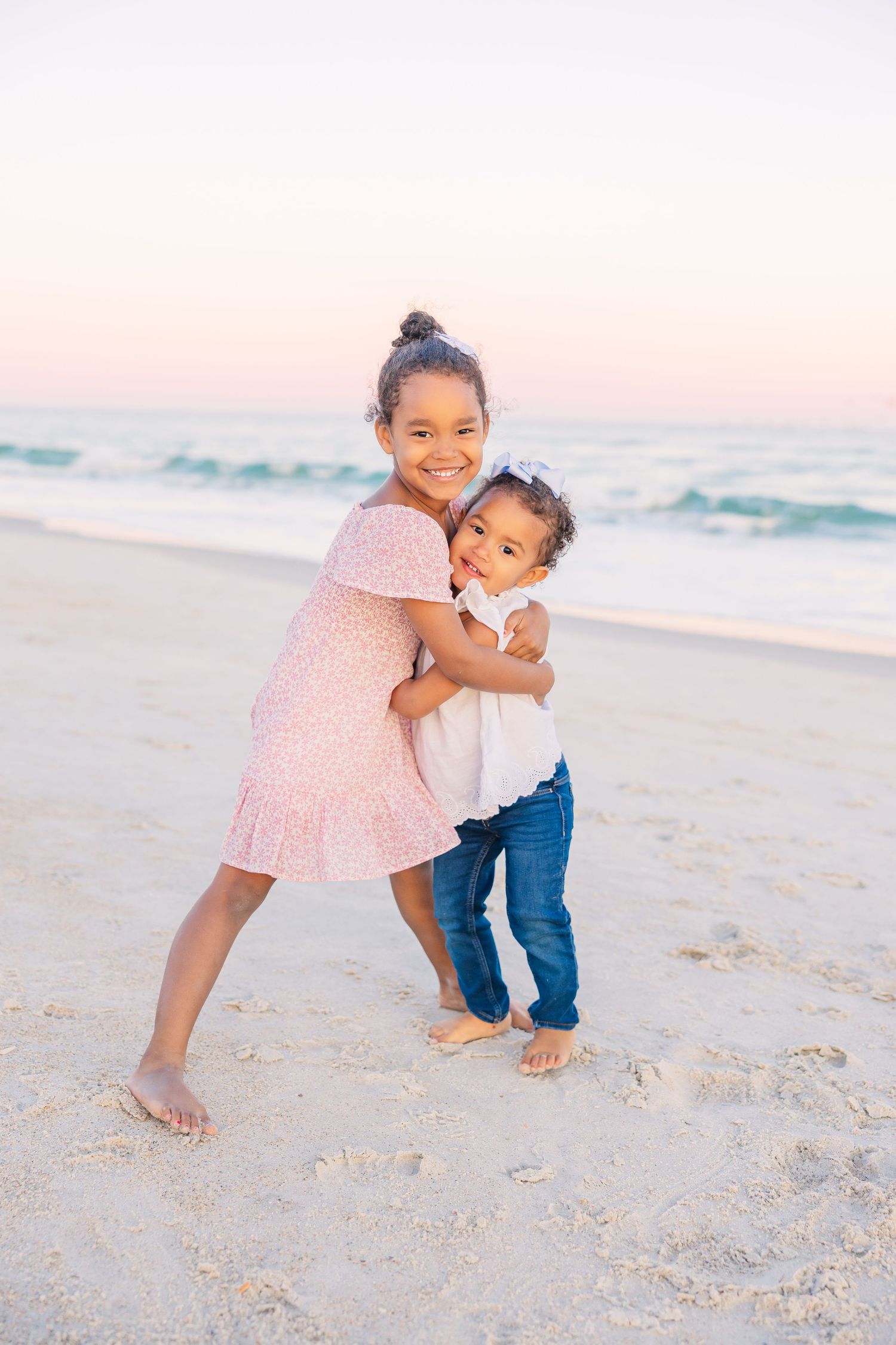 Children playing and hugging on white sandy beach during golden hour.
