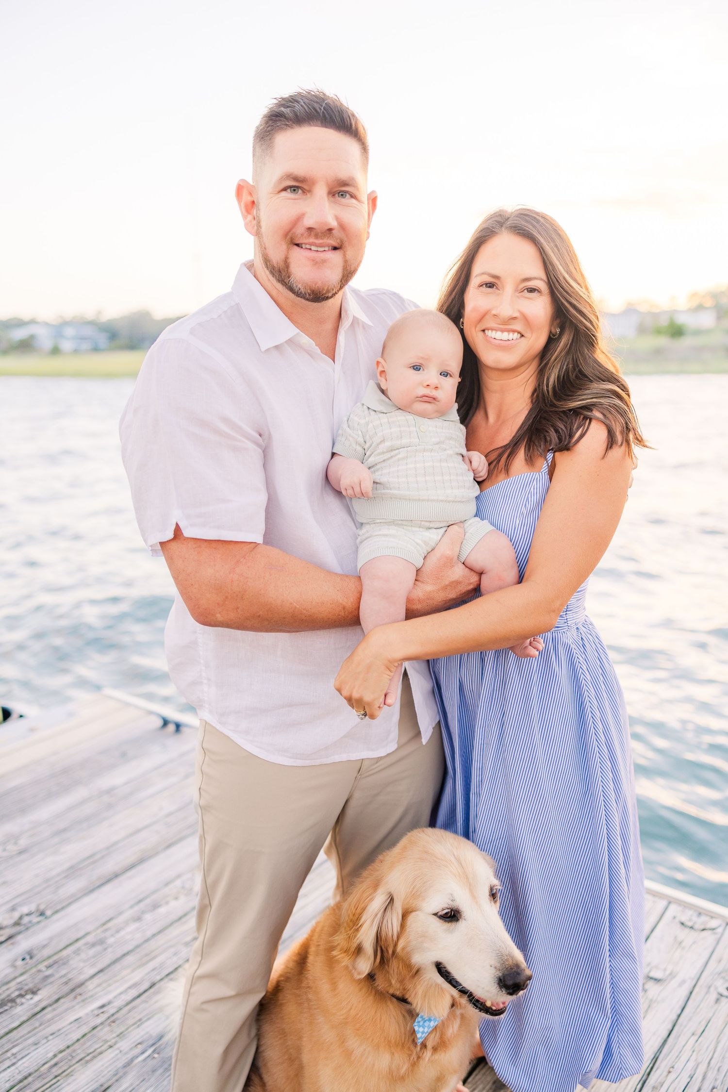 Family poses with their golden retriever on wooden dock during sunset.