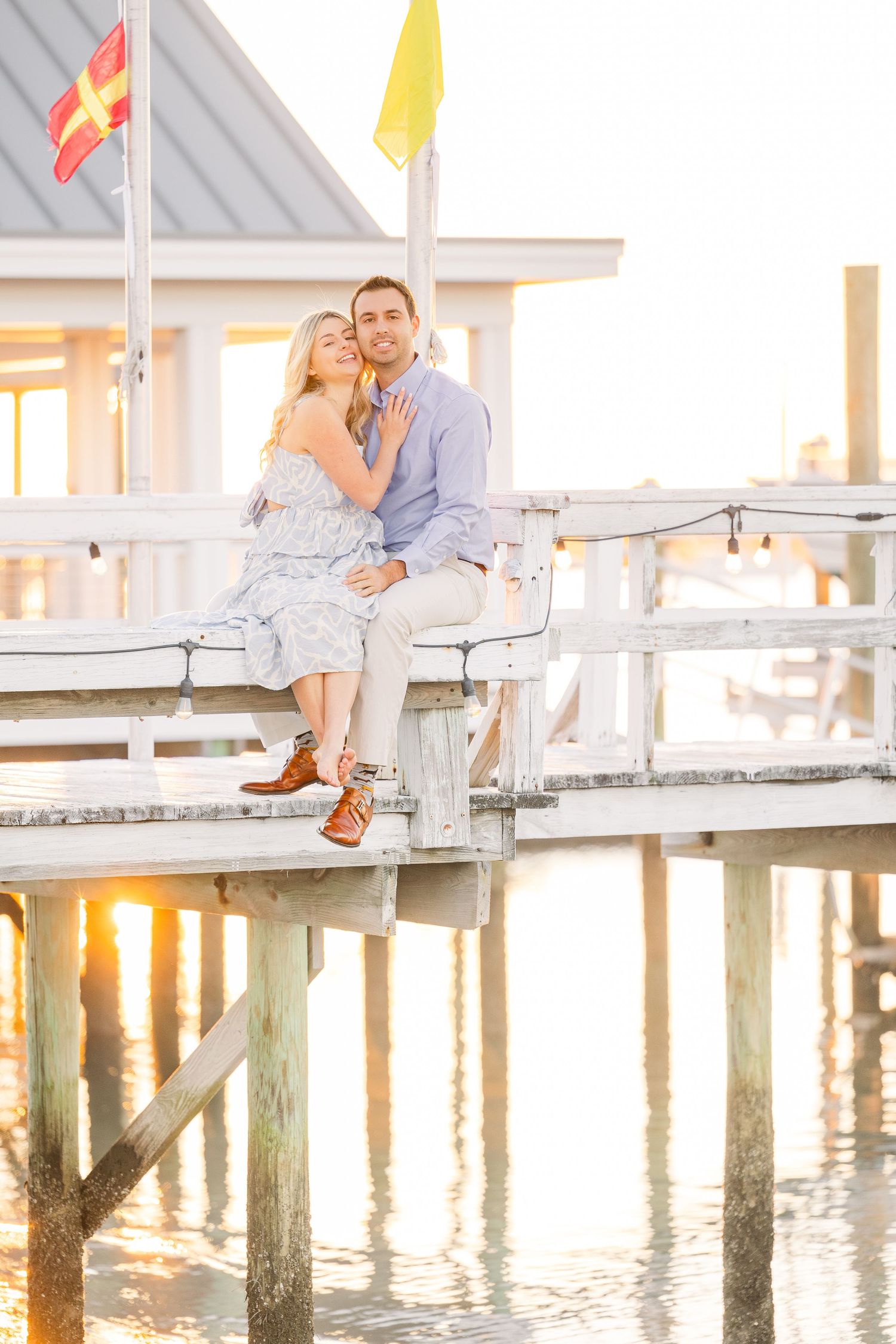 Intimate sunset portrait of couple sitting together on coastal dock with water reflections.