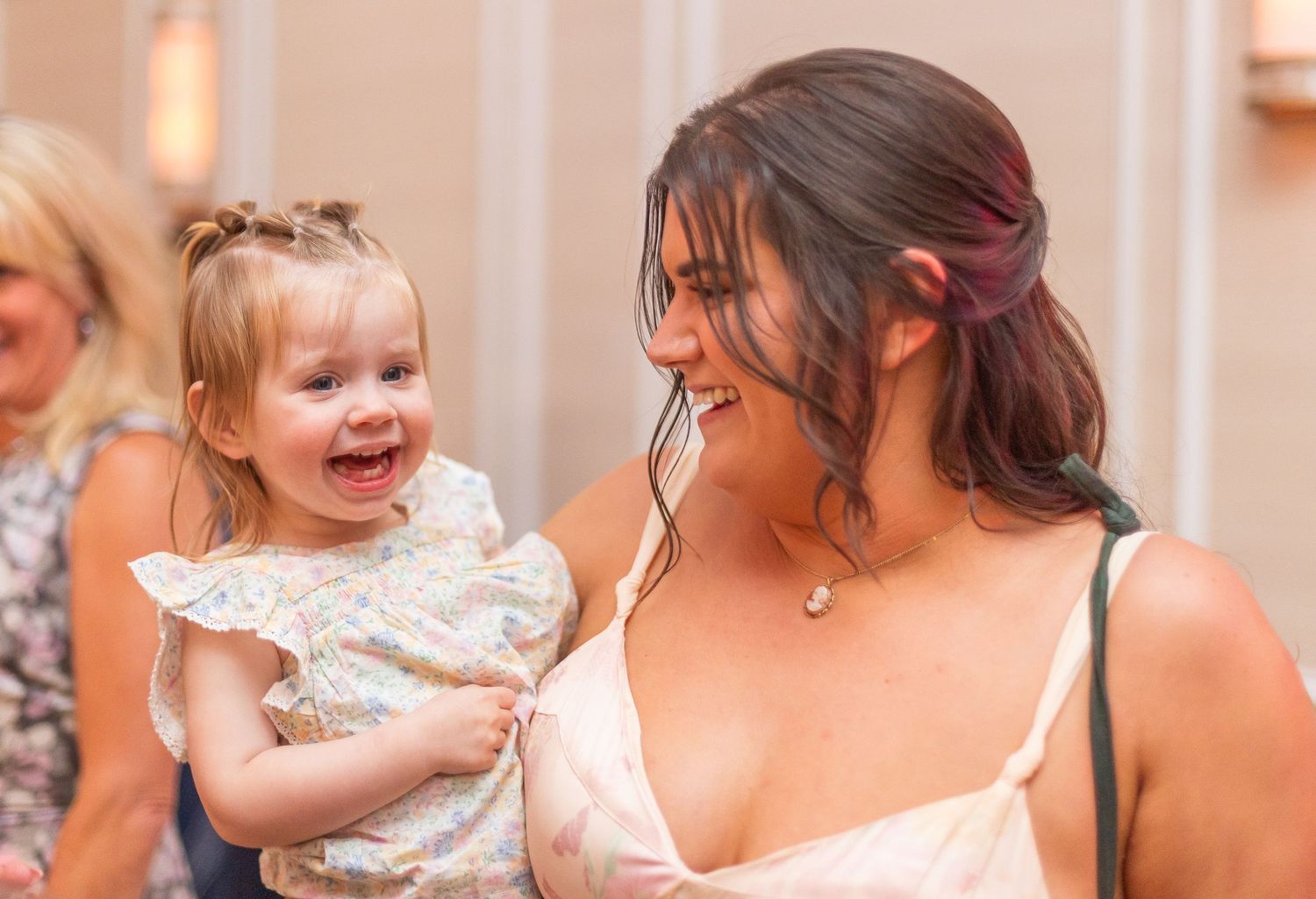 A heartwarming moment of laughter between a toddler in white and an adult at a formal event.