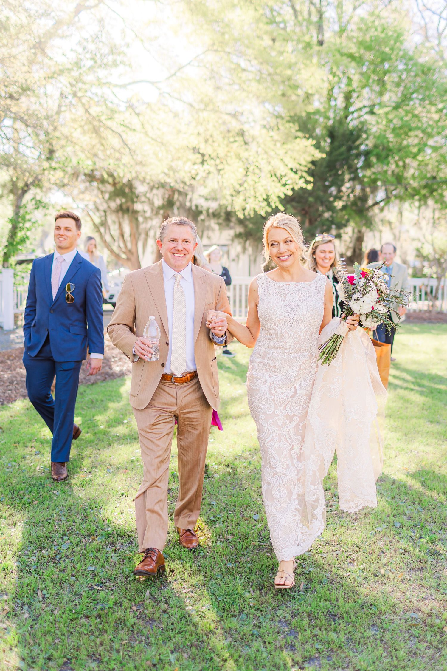 Wedding party walking and laughing together on grassy lawn during spring outdoor photo session.