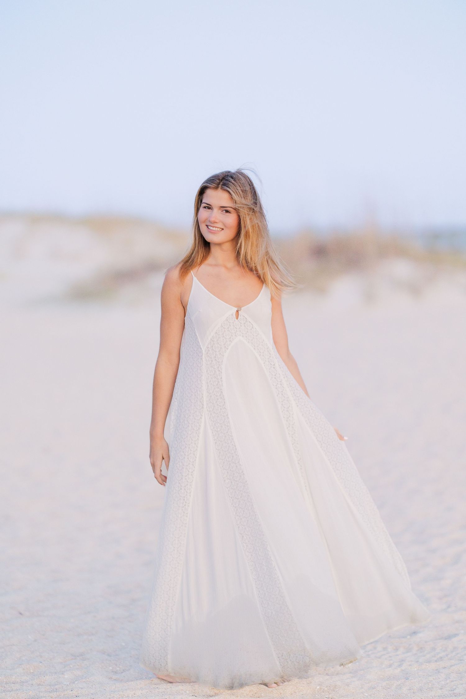 Ethereal beach photography with a flowing white dress against sand dunes.