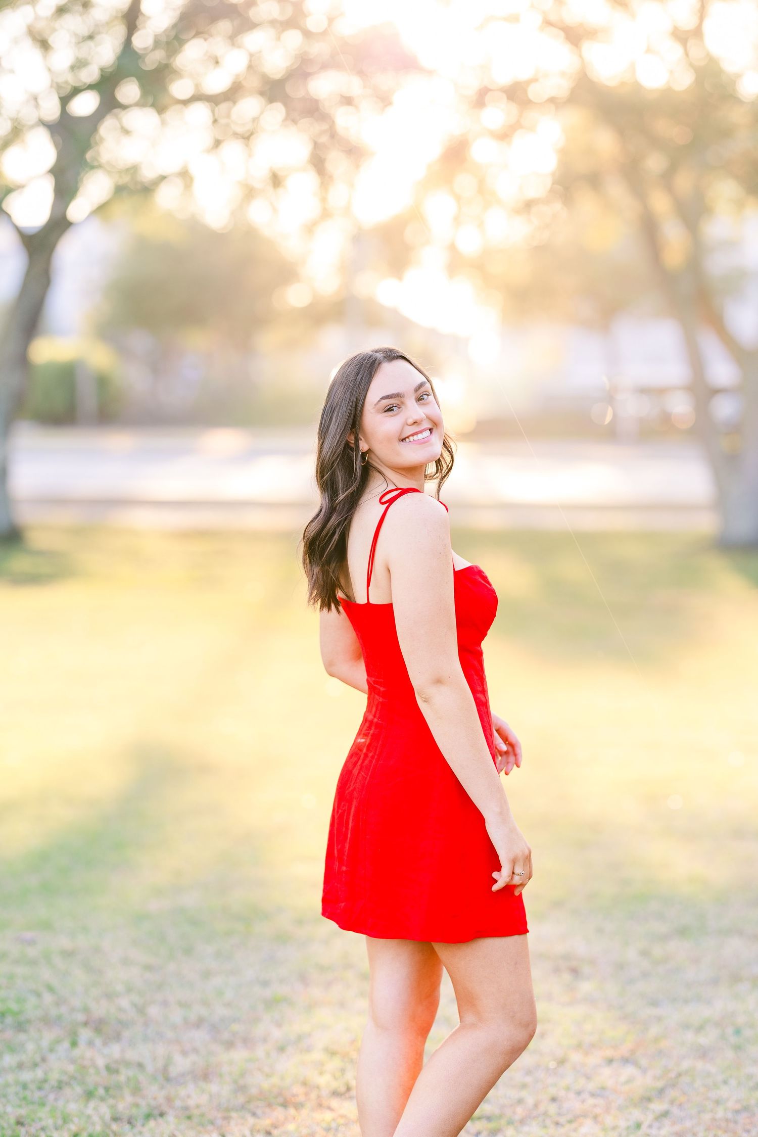 Sunset portrait in red dress with golden backlight and trees.