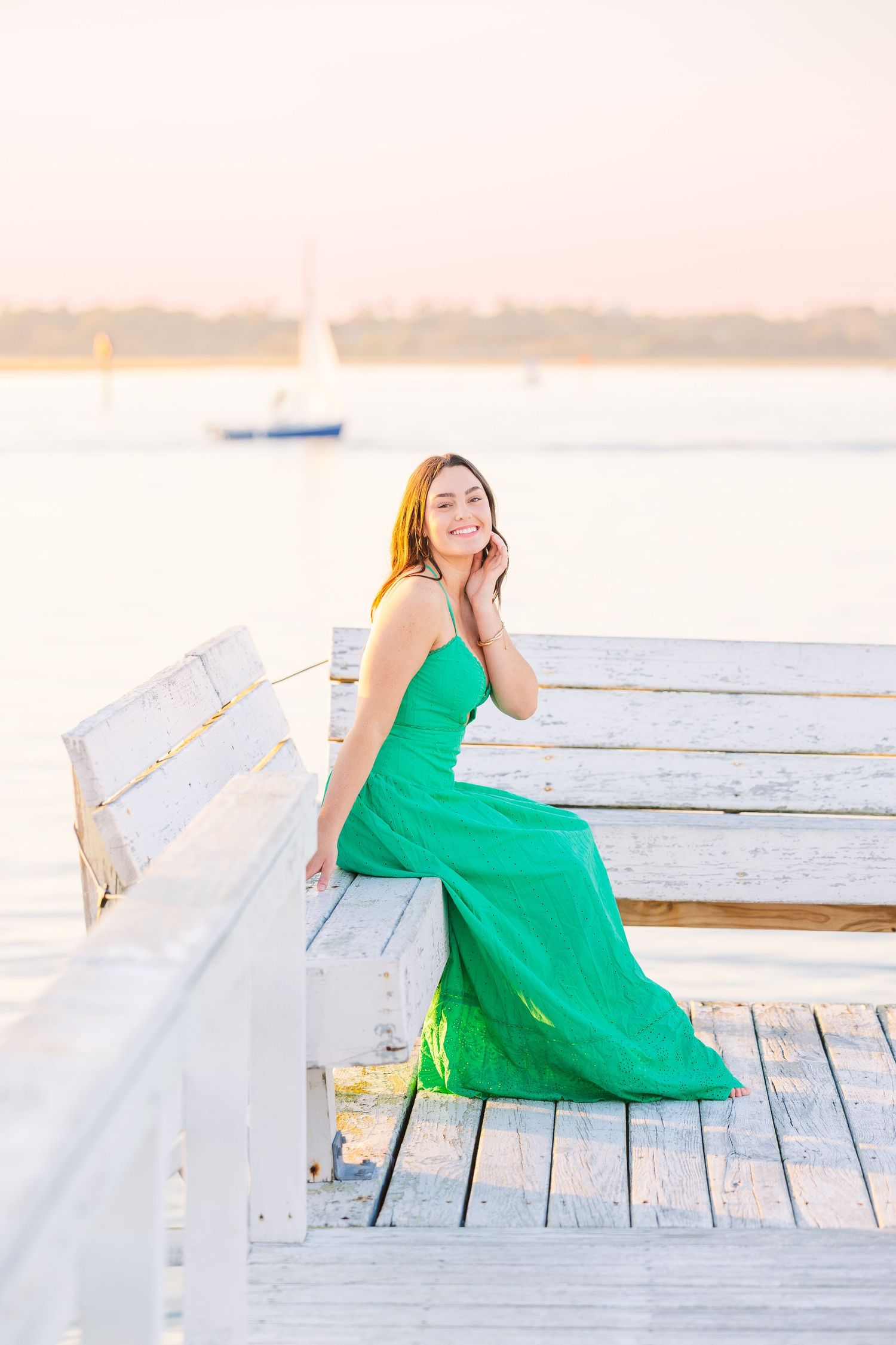 A flowing green dress creates a serene scene on a white dock at sunset.