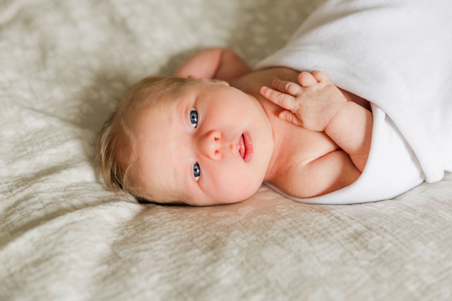 Artistic black and white portrait of infant resting on textured bedding.