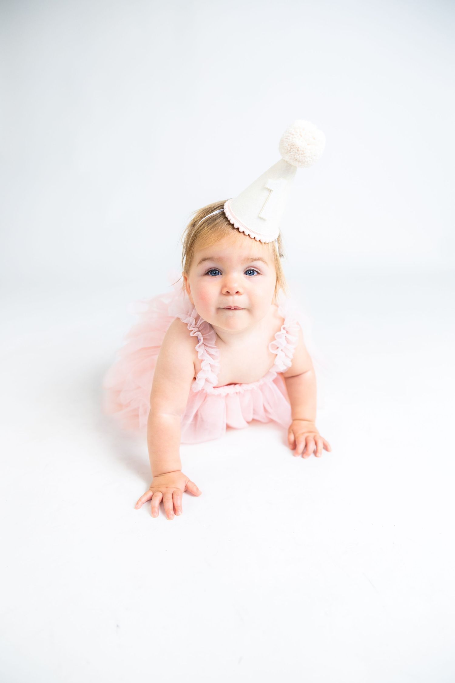 Baby in pink dress and bow posing on white background.