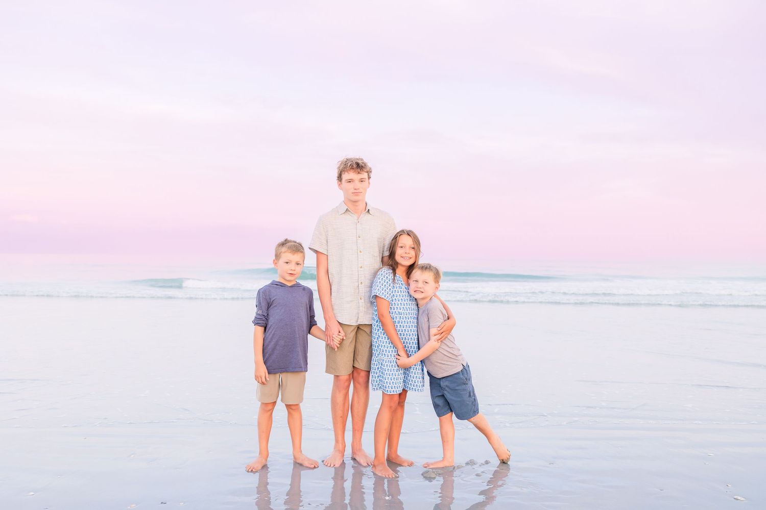 Beach family portrait with soft pastel sky and ocean waves in background.