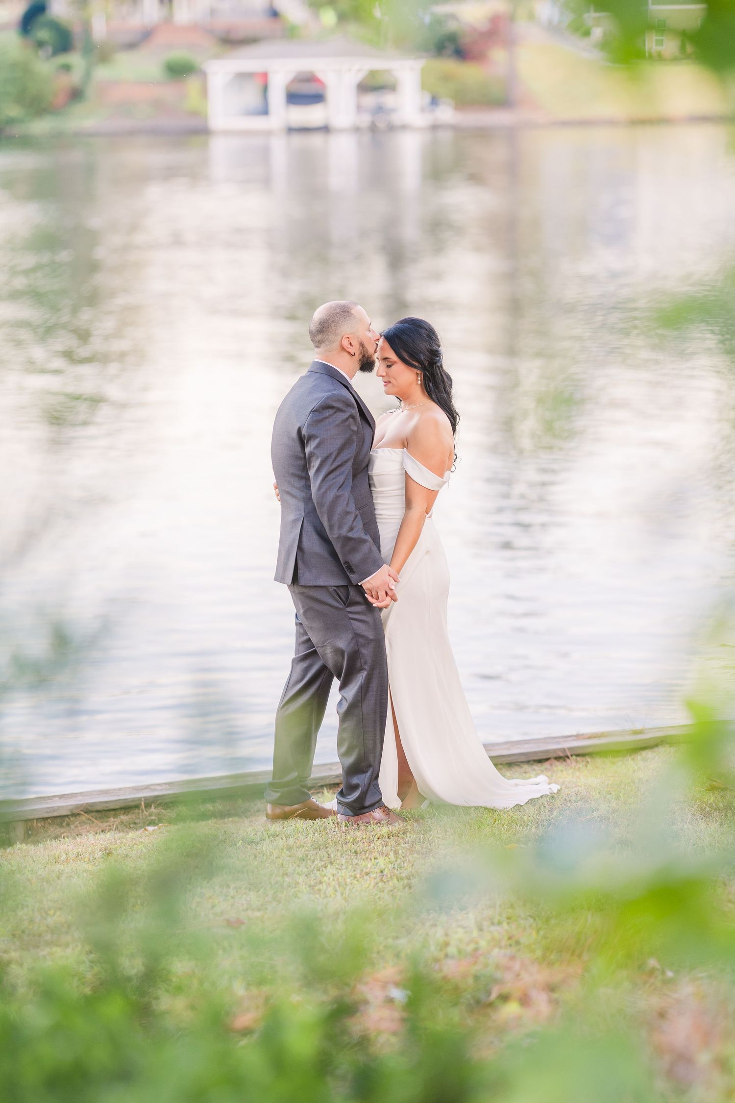 A couple shares an intimate moment near a lake with soft focus foliage framing the scene.