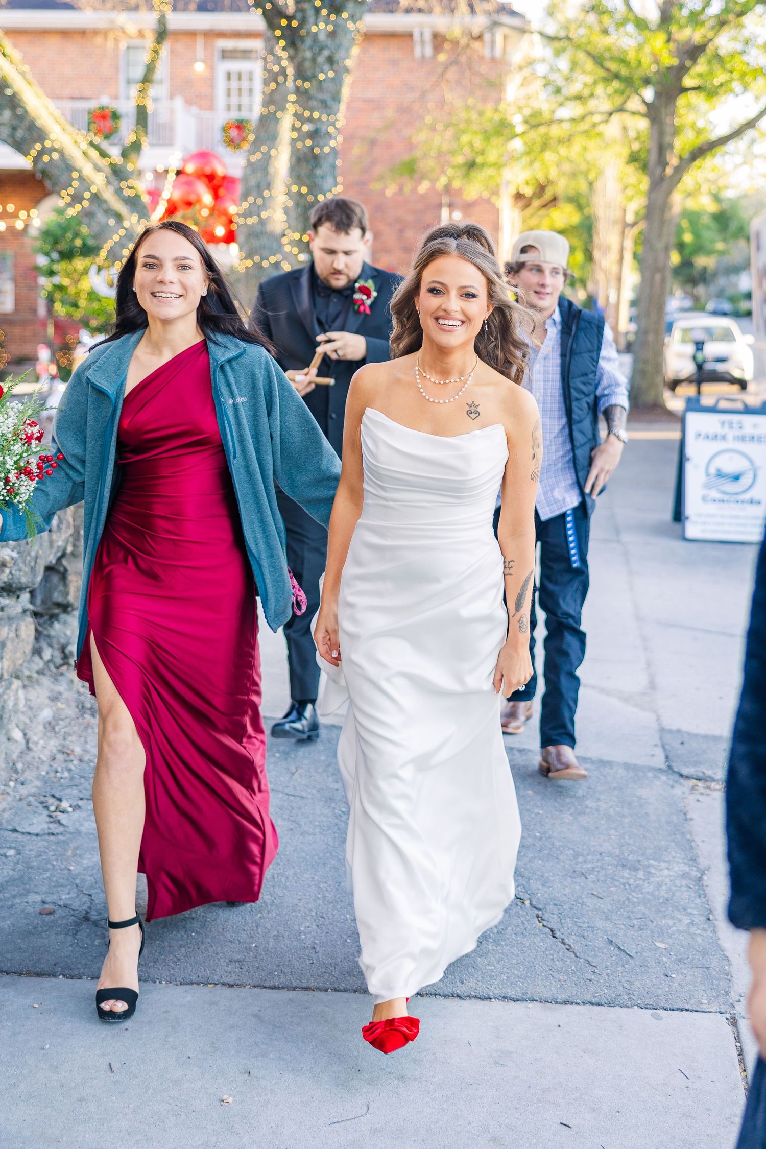 Wedding party walking down sidewalk with bride in white gown and bridesmaid in burgundy dress.