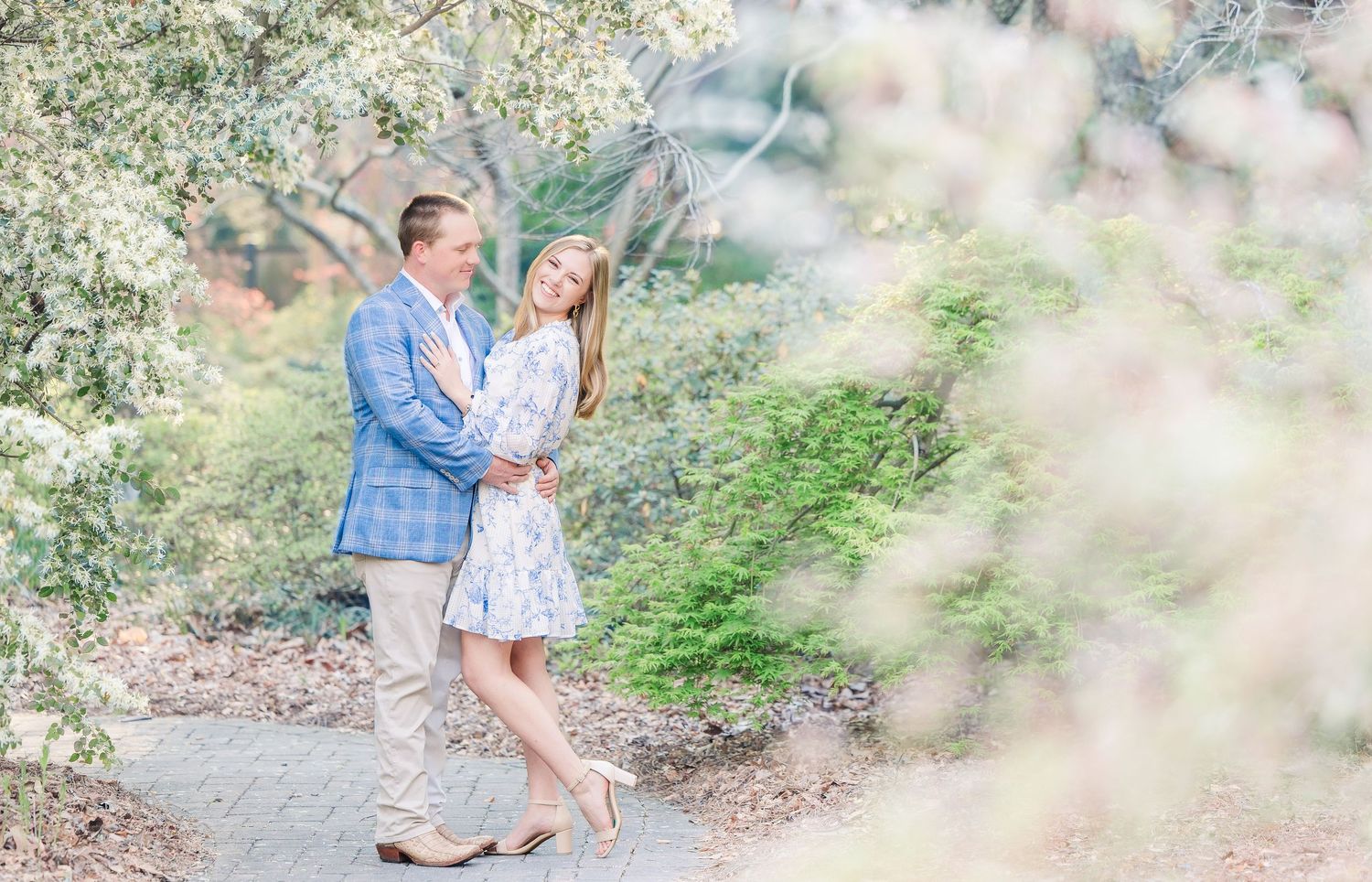 A romantic couple walks hand in hand along a scenic garden path surrounded by soft bokeh lighting effects.