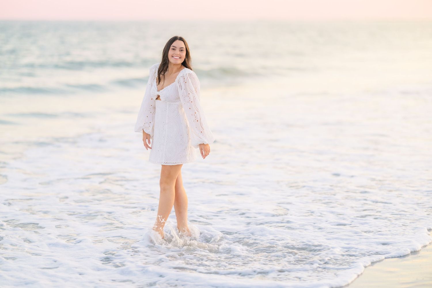 Dreamy beach portrait showing a white dress against gentle ocean waves at dusk.
