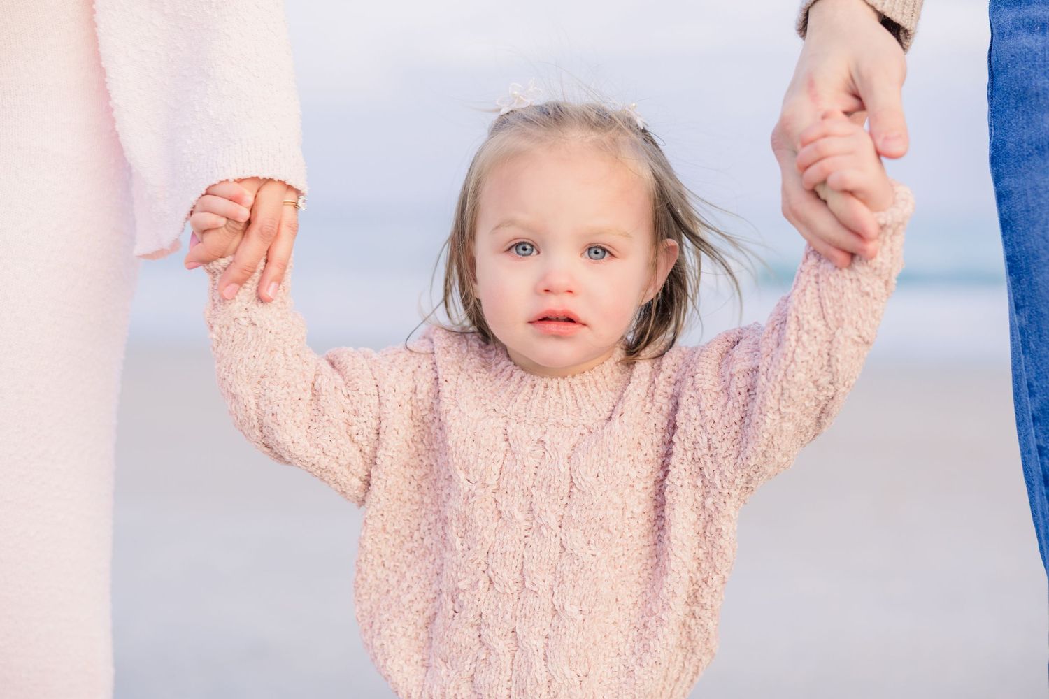 Child reaches up with both hands while playing on a misty beach.
