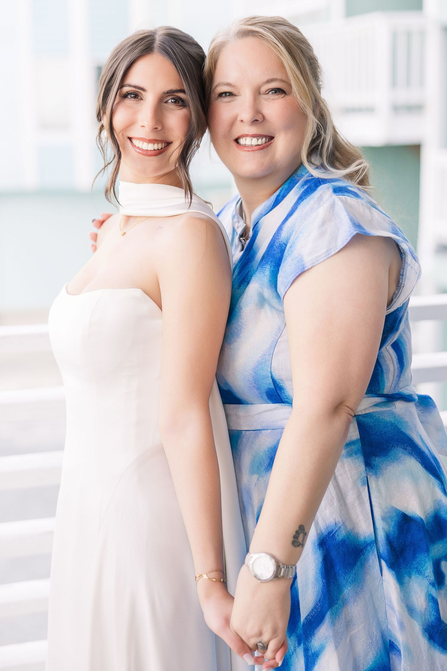 Bride in white gown and woman in blue floral dress smiling together at a beach wedding in Carolina Beach near Wilmington, NC.