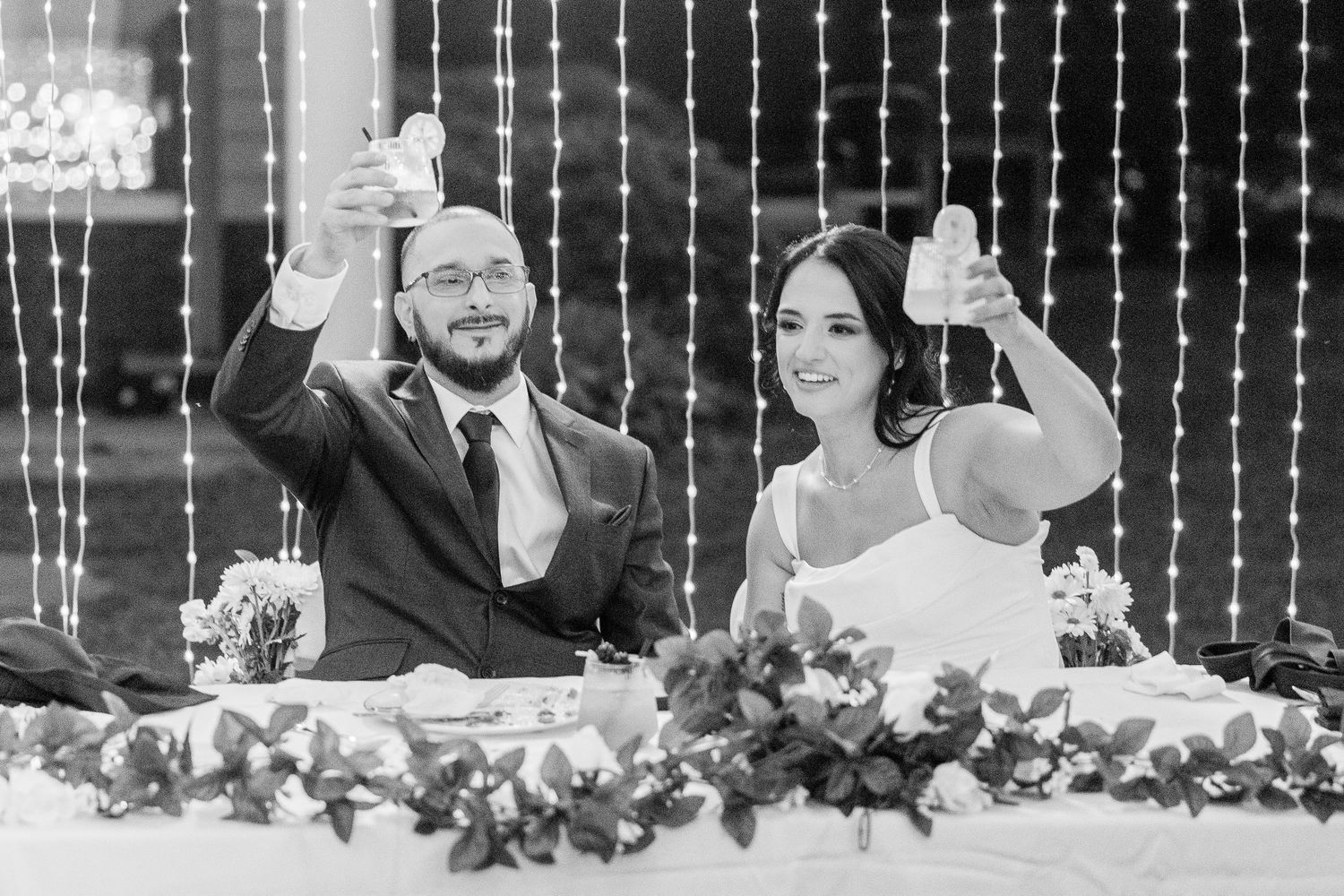 Guests celebrate with raised glasses during a wedding reception under twinkling string lights wedding groom bride lake Gaston photographer