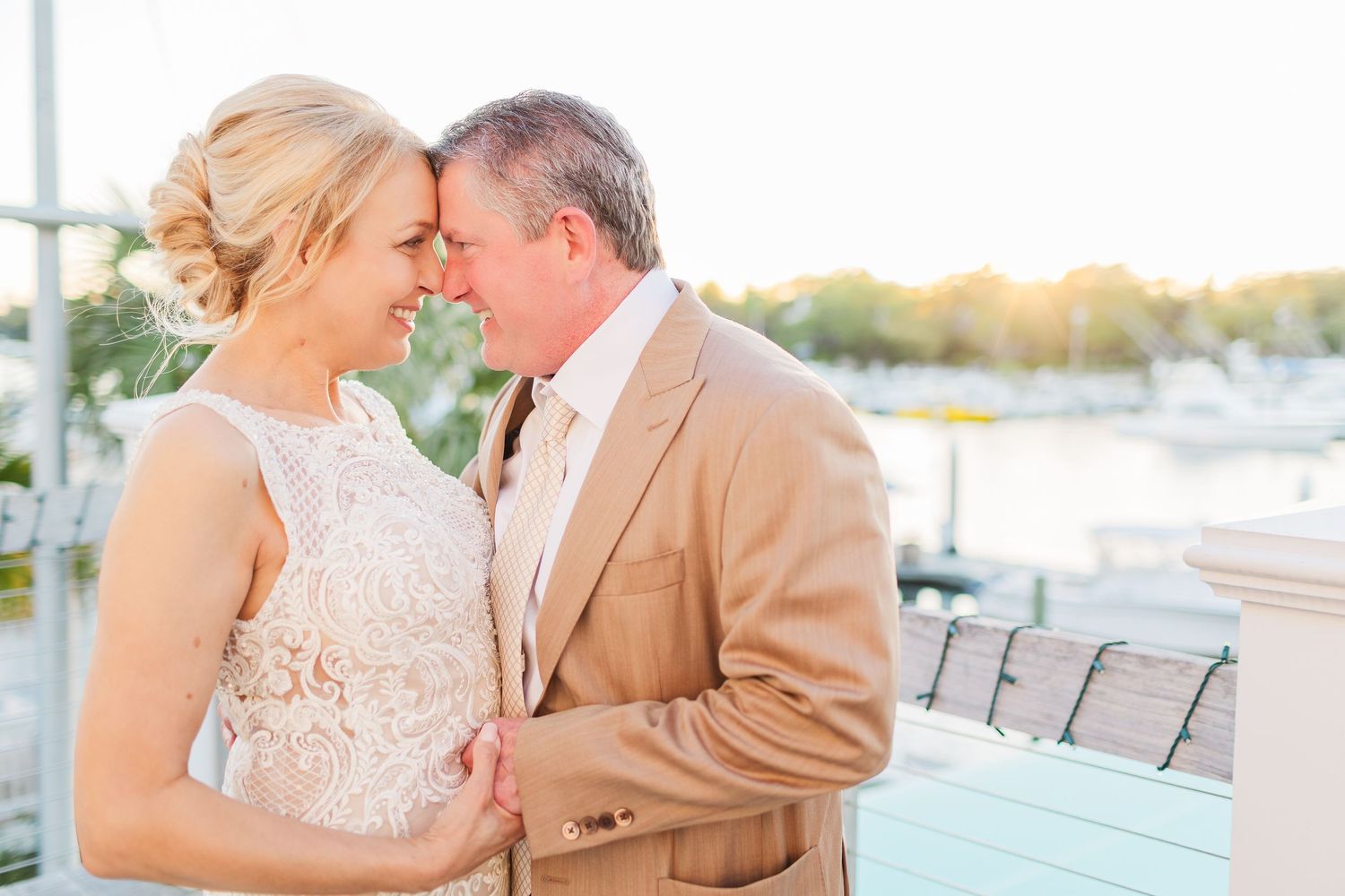 Couple shares a romantic moment on a waterfront deck during sunset with boats in the marina background.