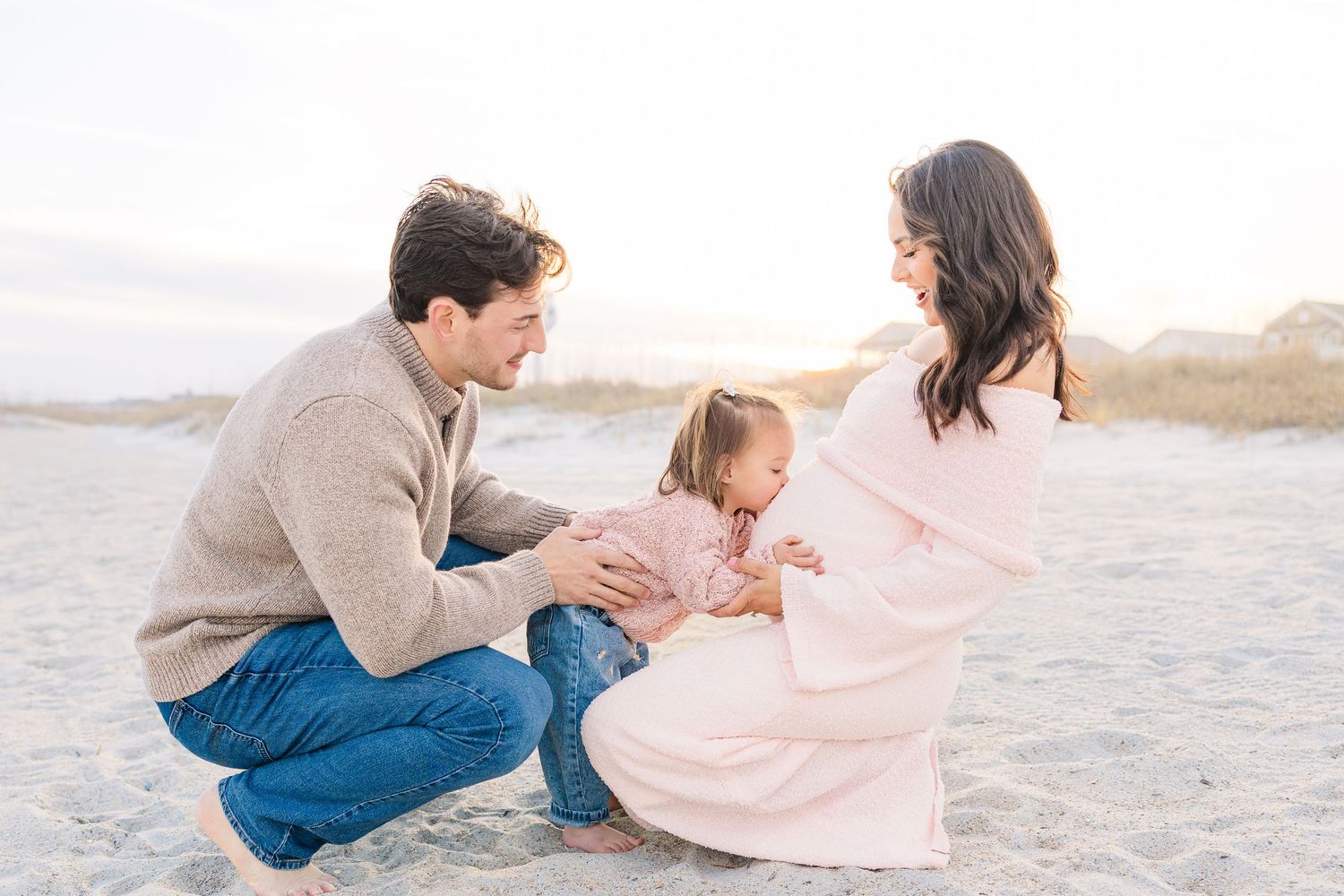 Family sitting together on beach sand during golden hour wearing coordinated neutral colors.