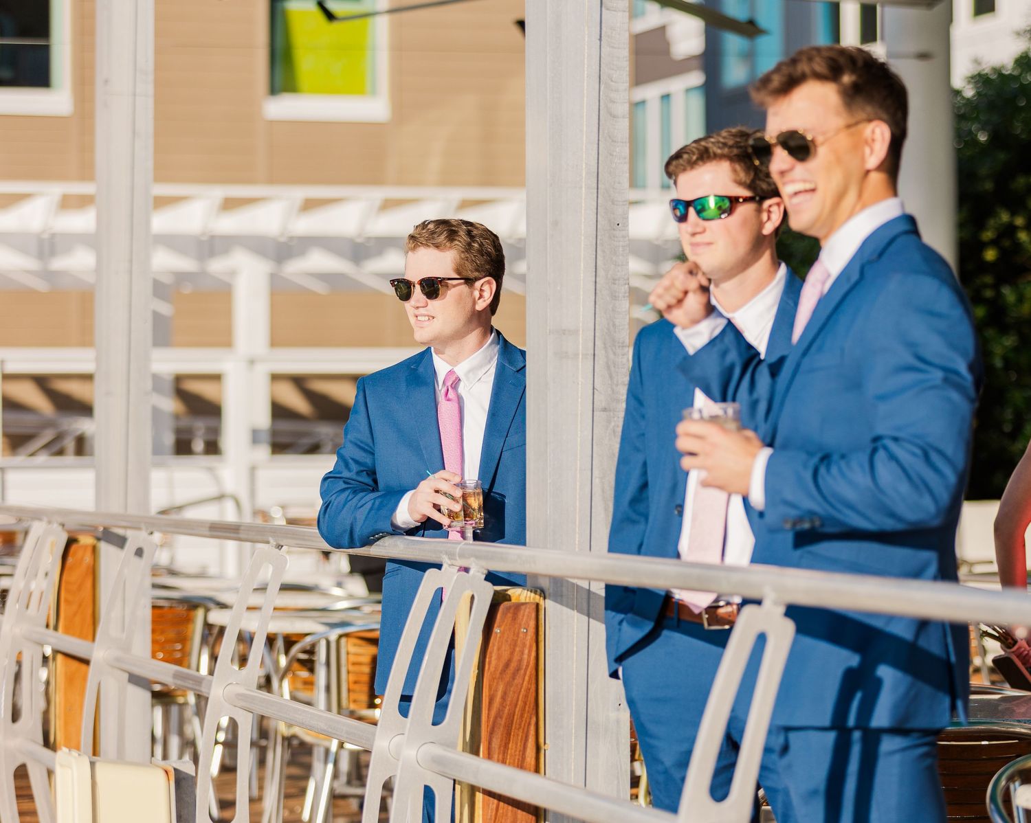 Groomsmen in blue suits and sunglasses celebrate on a patio during a wedding reception.
