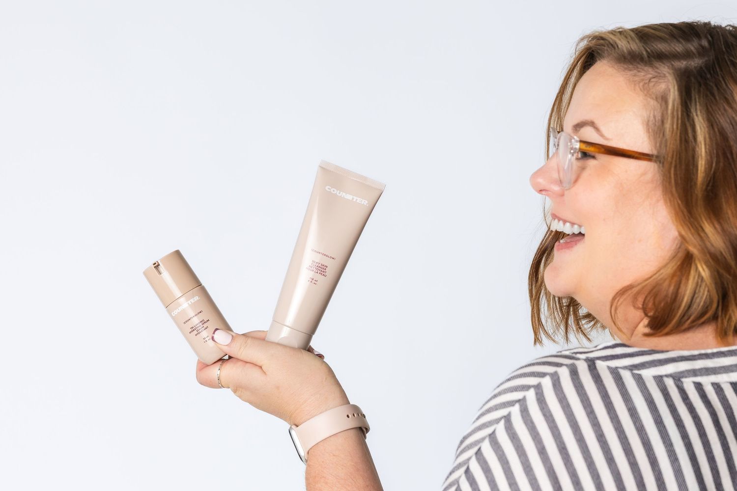 Person wearing striped shirt holding beauty products while smiling.