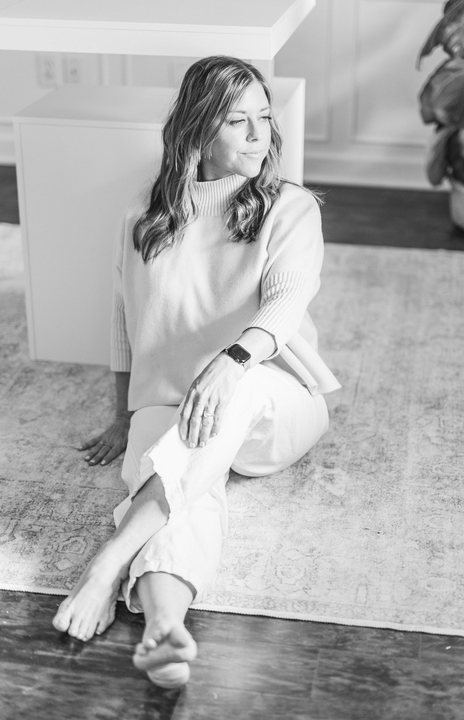 Monochrome image of someone in cozy sweater sitting casually on floor against white wall.