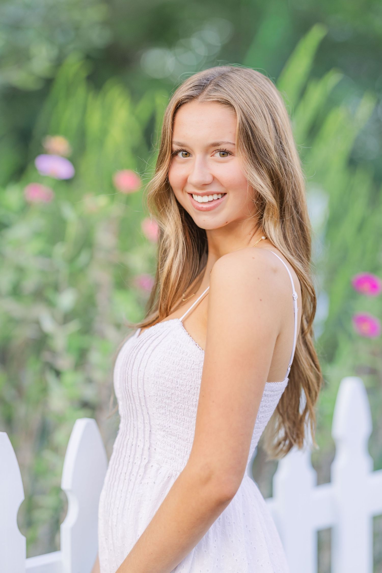 Outdoor portrait by a white picket fence surrounded by greenery.