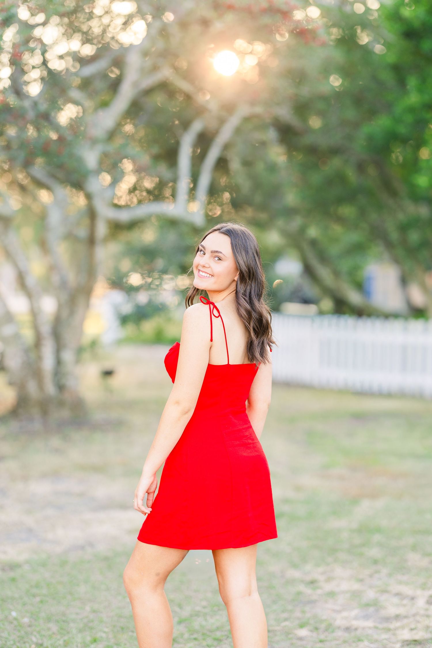 A bright red dress catches the golden sunlight in an outdoor garden setting.
