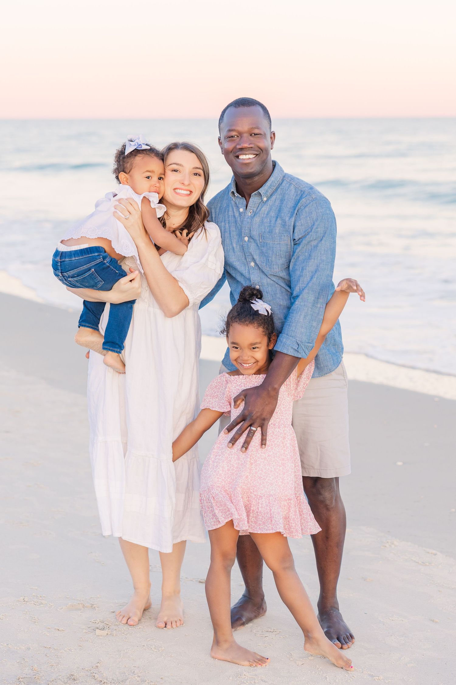 Family portrait on beach with ocean waves and sunset in background.