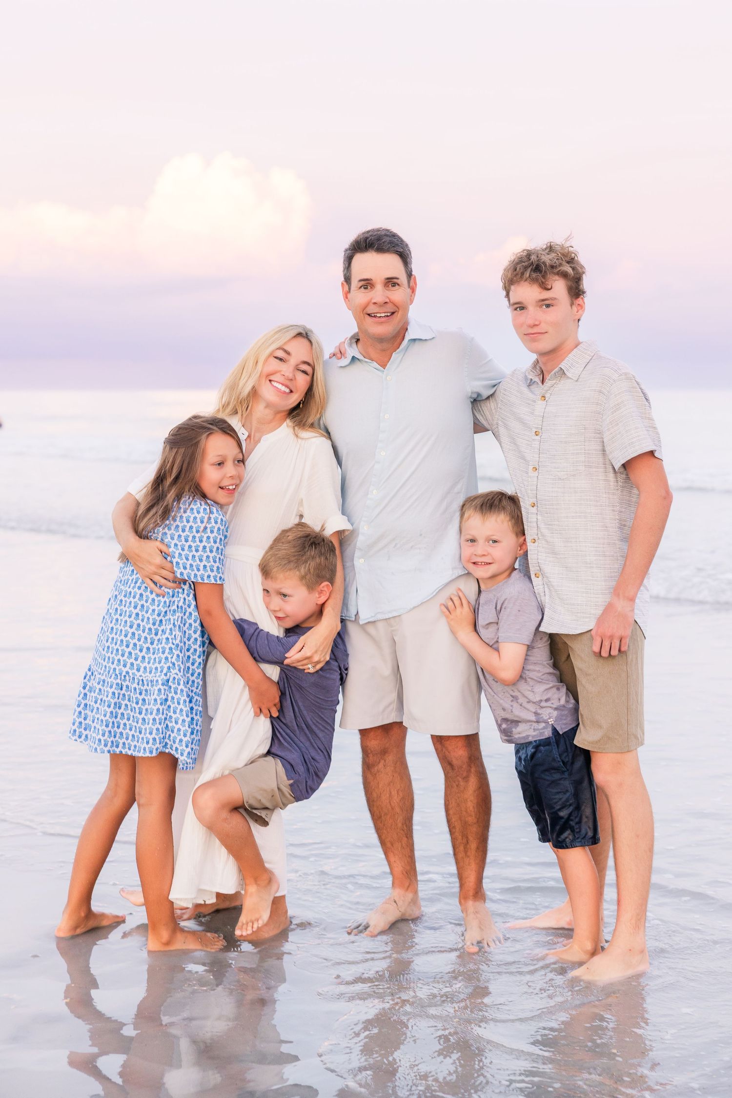 A joyful family moment captured while standing in shallow ocean water during sunset.