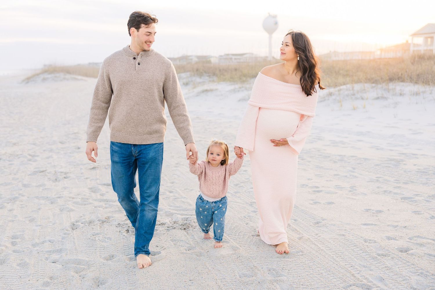 Family walking along sandy beach at sunset wearing coordinated casual outfits.
