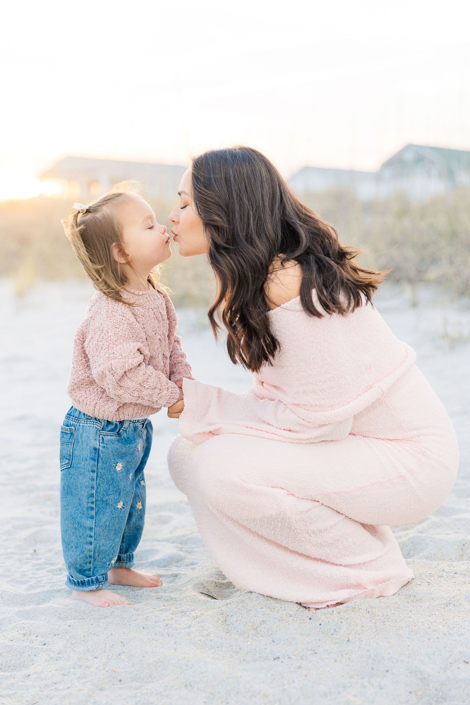 Parent and child play together on sandy beach wearing matching pink tops.