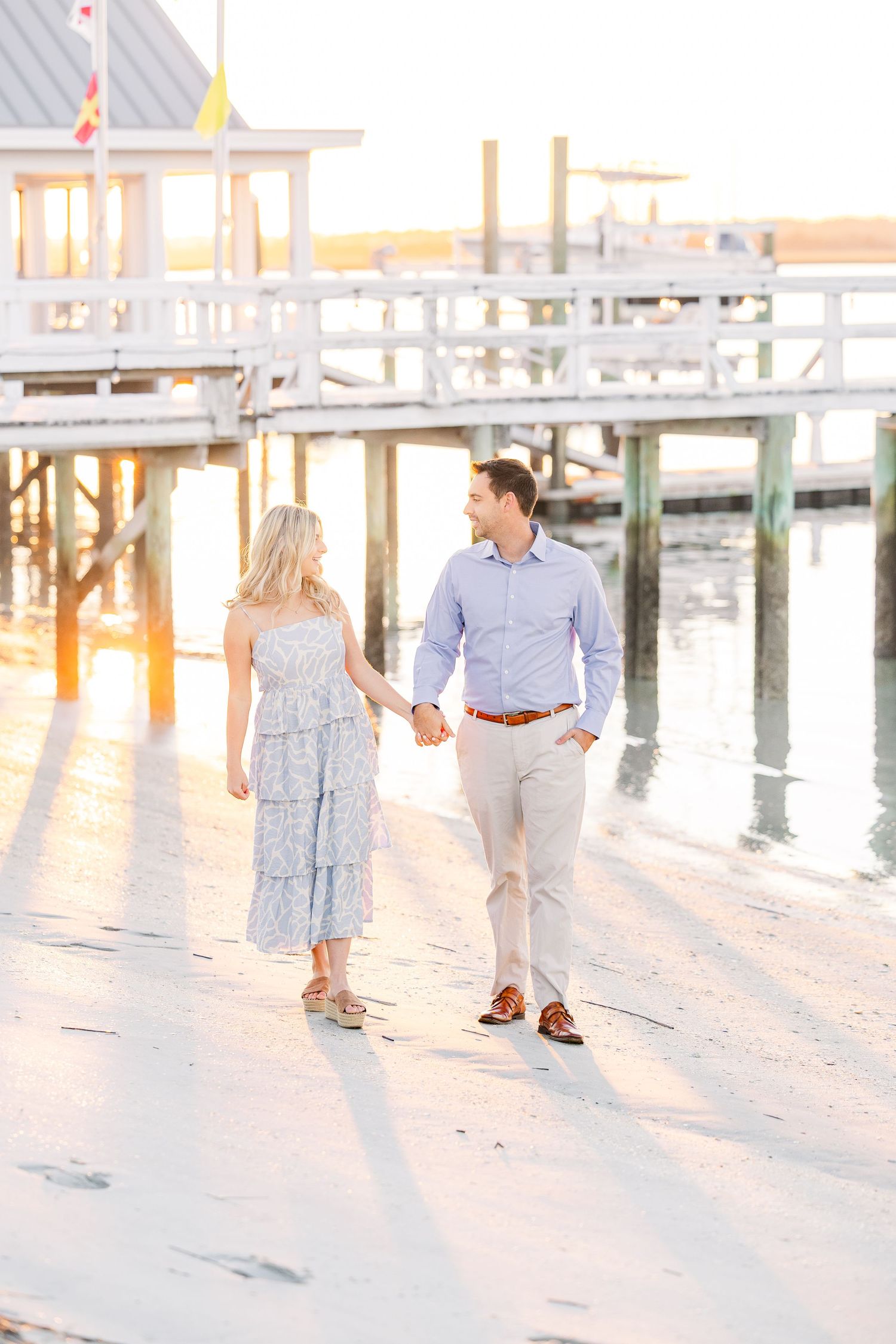 Couple walking hand in hand on waterfront boardwalk during sunset.
