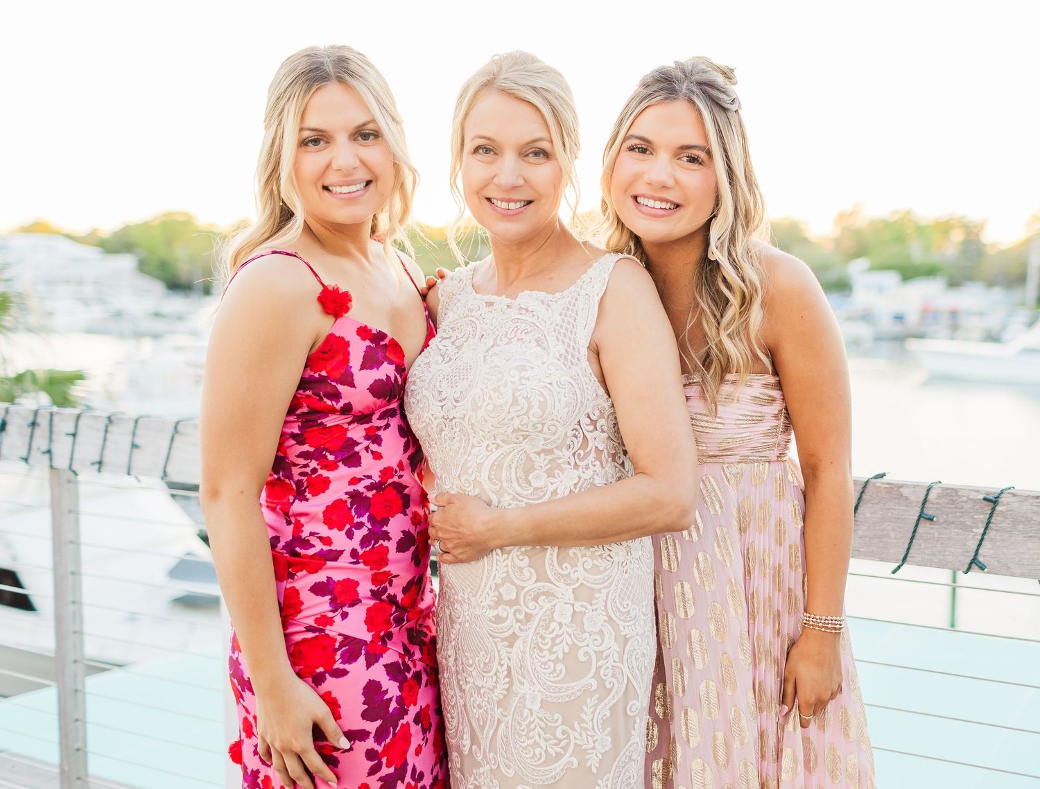 Wedding party in pink and floral dresses pose together on waterfront deck.
