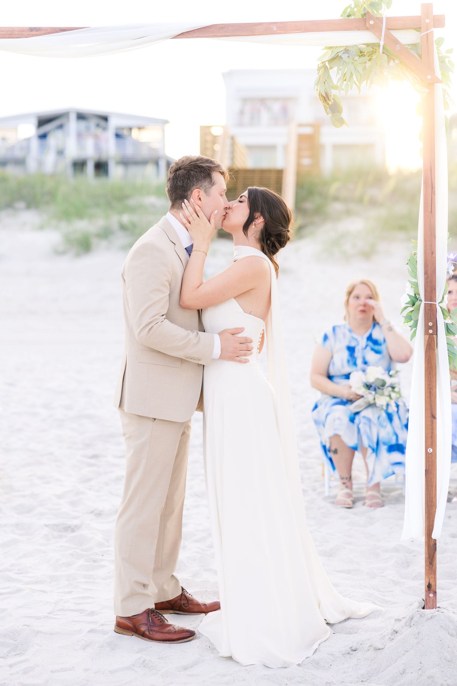 Bride and groom share their first kiss under a wooden arch on the beach at golden sunset in Carolina Beach near Wilmington, NC.