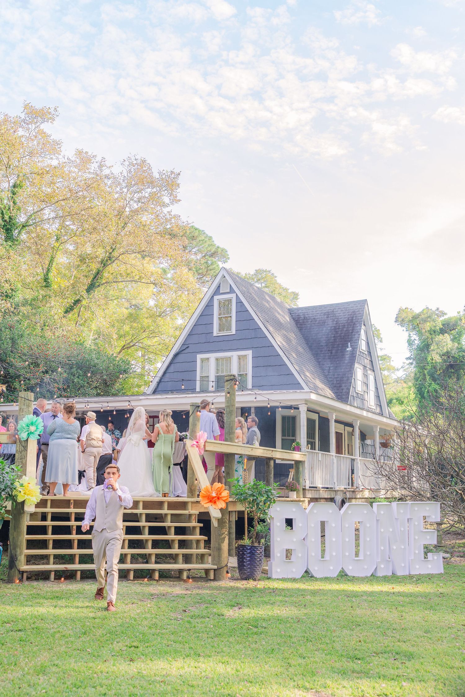 Grey cottage-style house with wooden deck serves as backdrop for outdoor wedding celebration wedding groom bride wilmington photographer