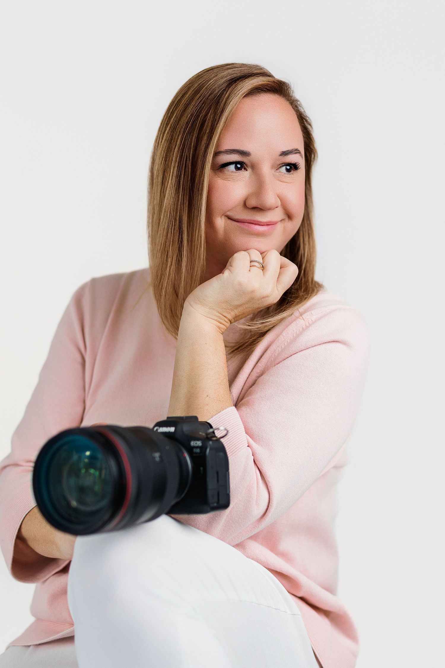 Professional photographer in pink sweater poses with camera against white background.